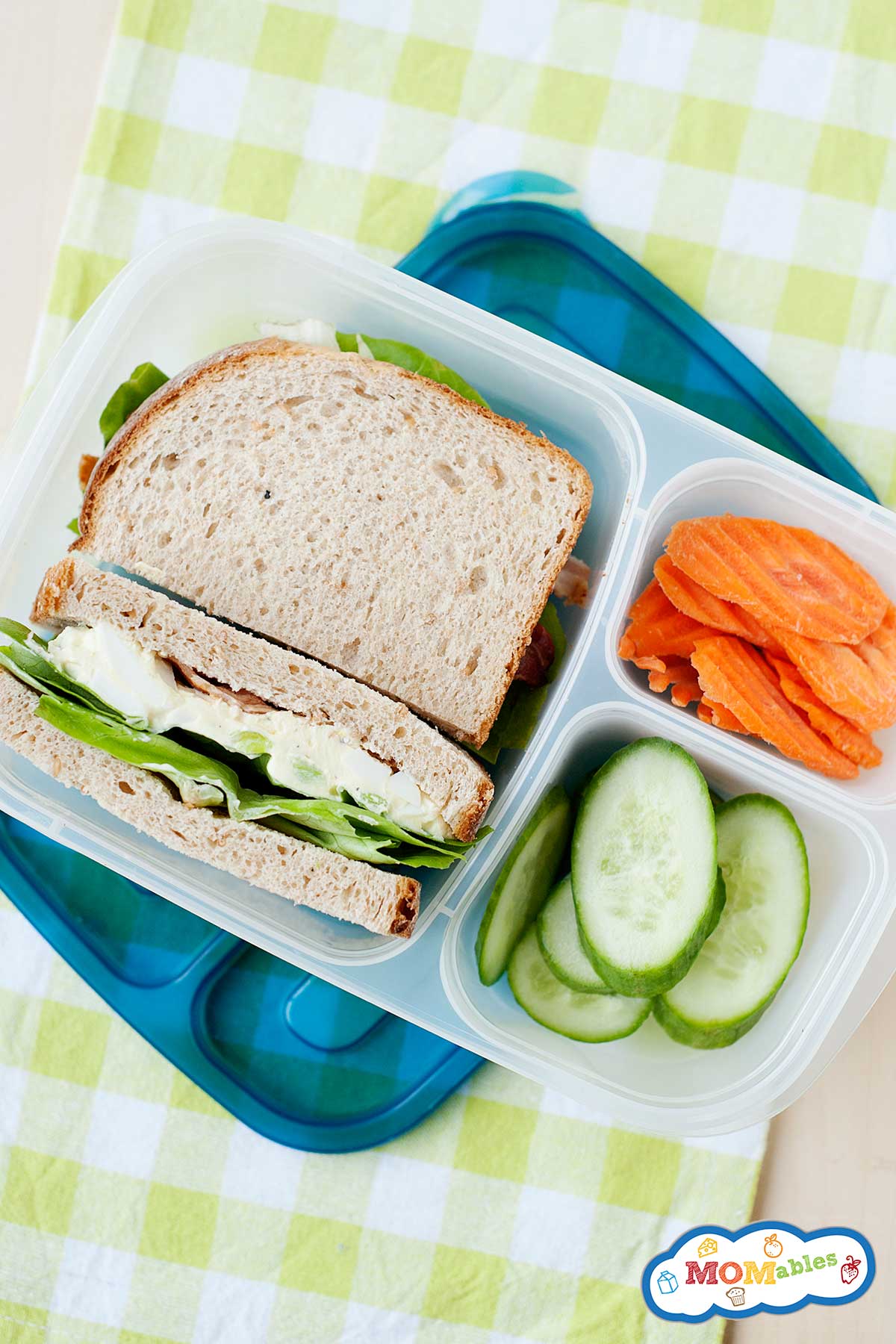 an egg salad sandwich packed in a lunch container with sliced veggies