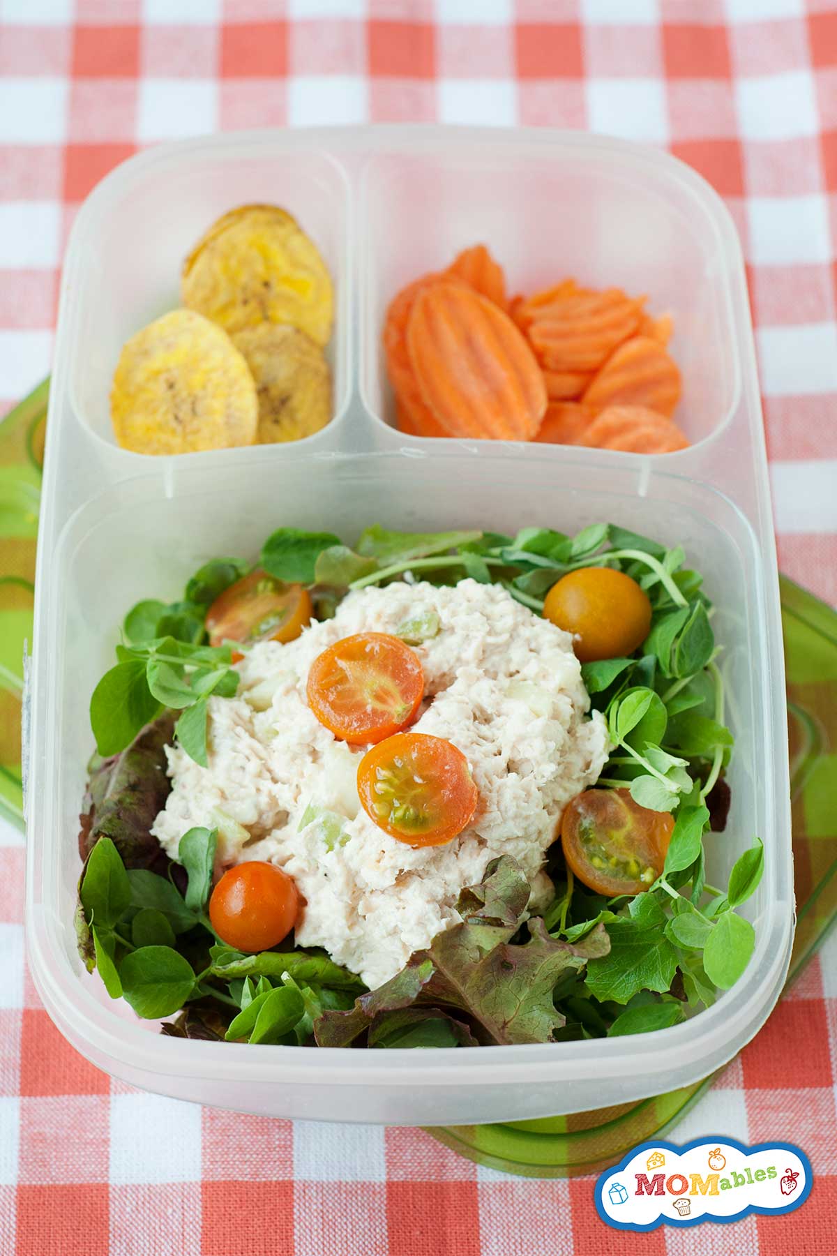 Chicken salad over a bed of greens, topped with grape tomatoes, and packed into a lunch container with banana chips and carrots.