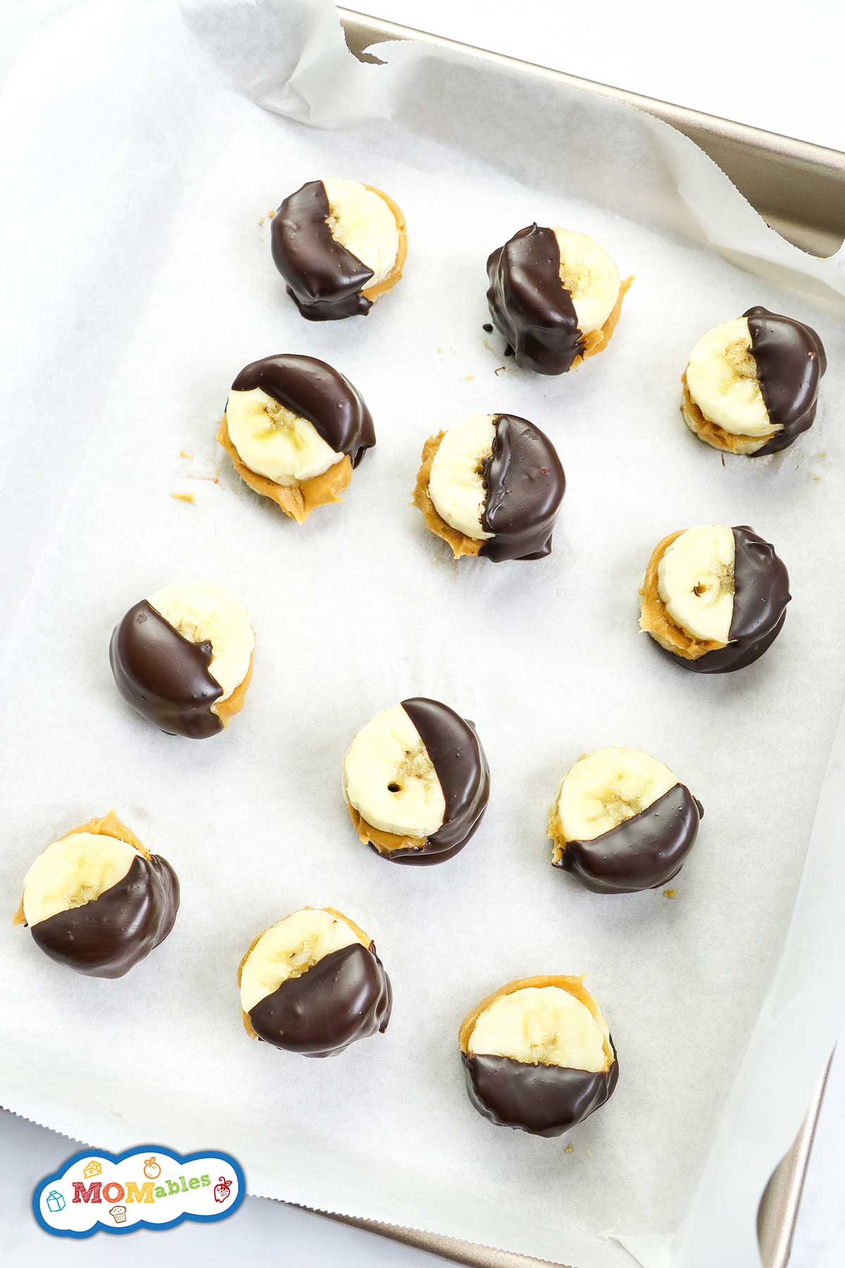 frozen banana bites dipped in chocolate and lined up on a baking sheet