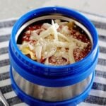 A thermos container filled with lasagna and topped with Mozzarella and Parmesan cheese