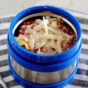 A thermos container filled with lasagna and topped with Mozzarella and Parmesan cheese