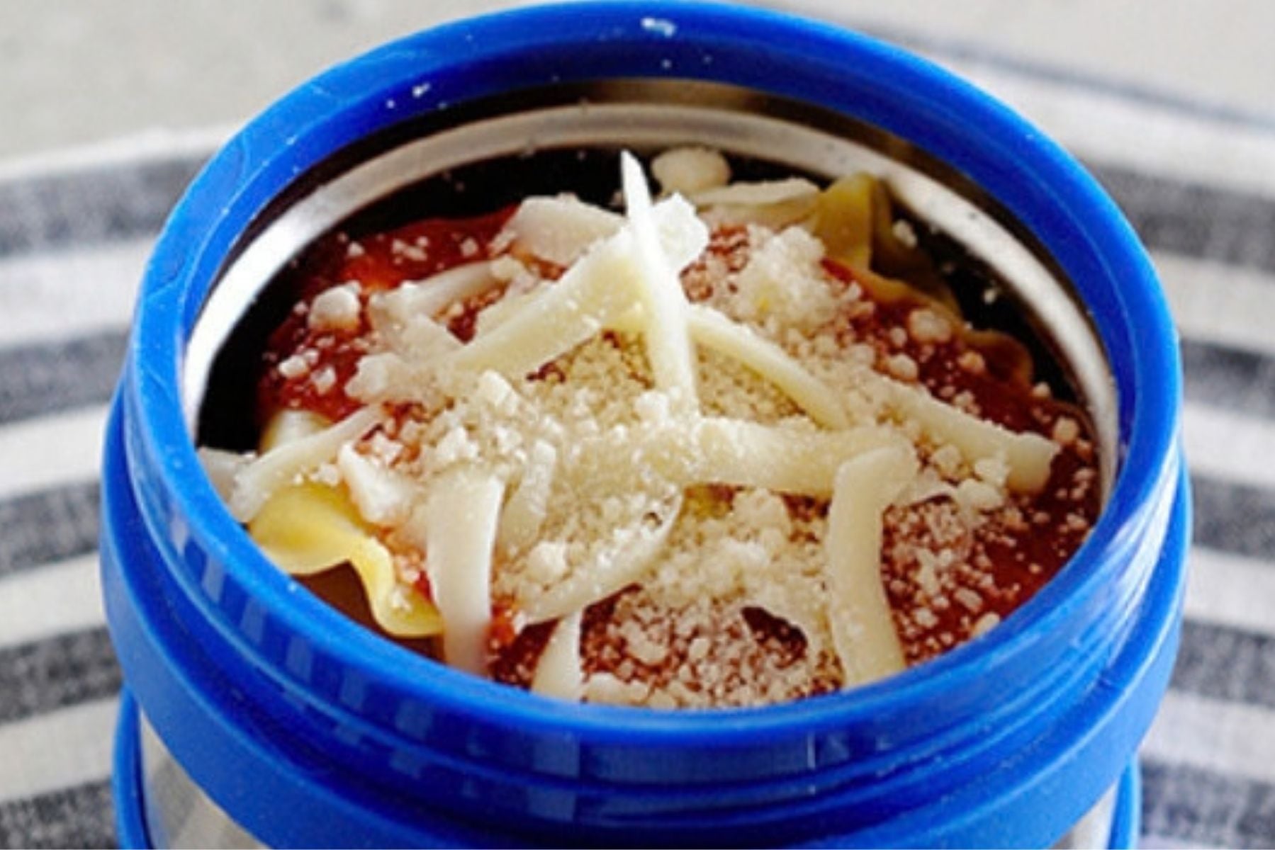 A thermos container filled with lasagna and topped with Mozzarella and Parmesan cheese