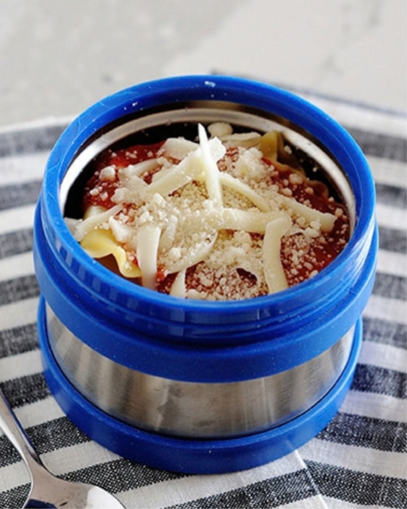 A thermos container filled with lasagna and topped with Mozzarella and Parmesan cheese