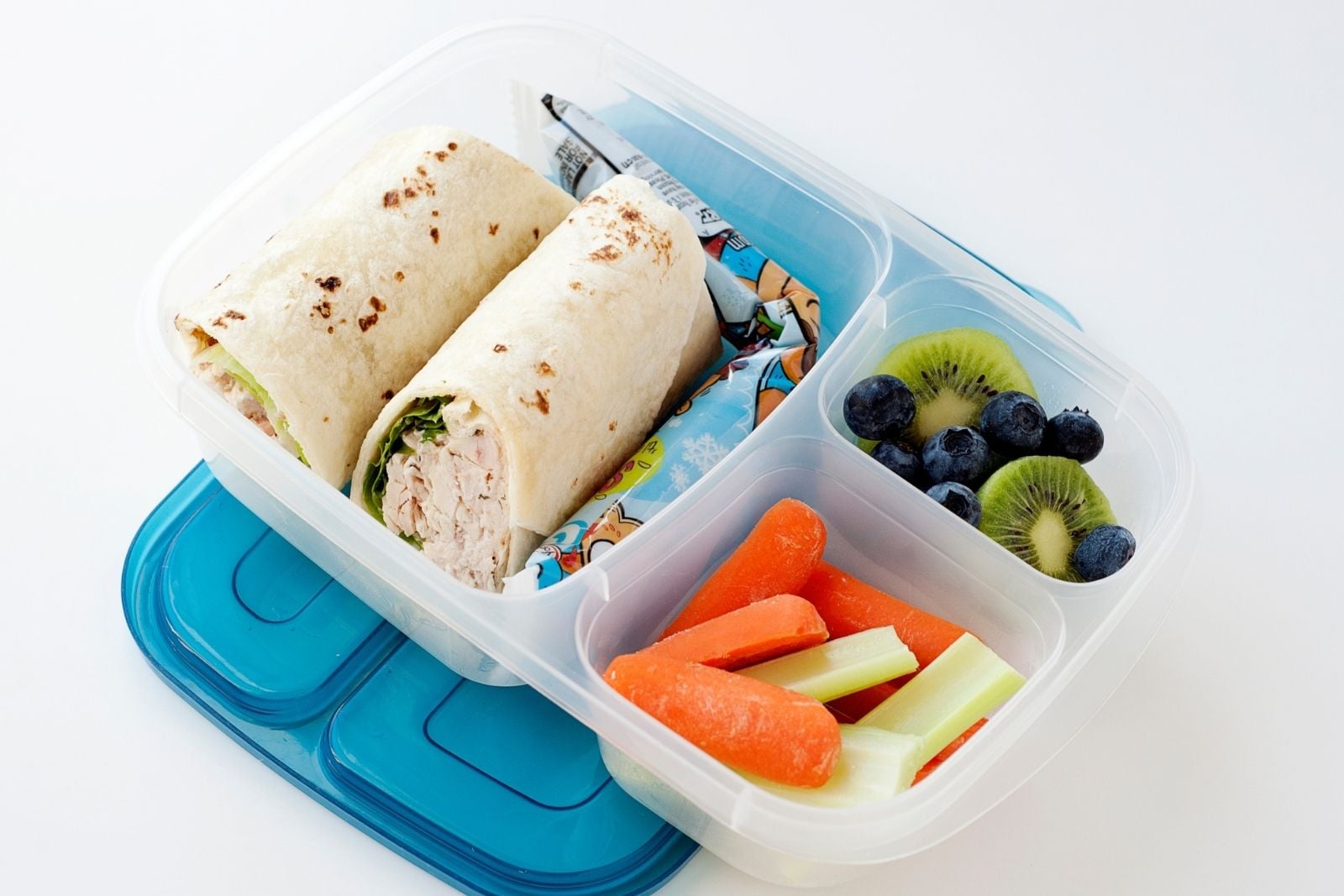 A chicken ranch wrap cut in half and packed into a lunch container with yogurt pack, fresh fruit, and veggies.