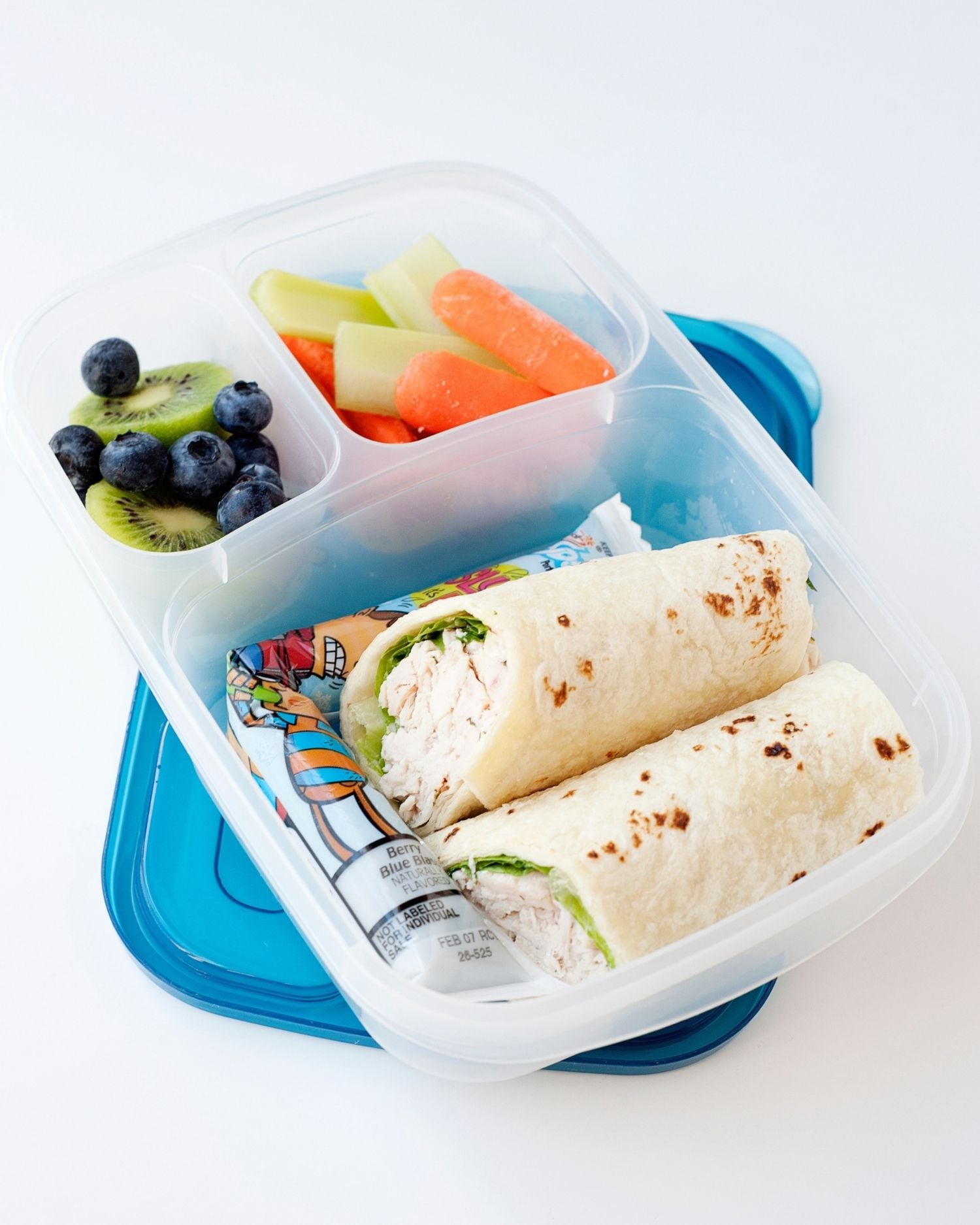 A chicken ranch wrap cut in half and packed into a lunch container with yogurt pack, fresh fruit, and veggies.