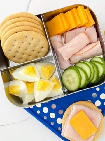 bento box with crackers, hard-boiled eggs, cucumber, turkey and cheese.