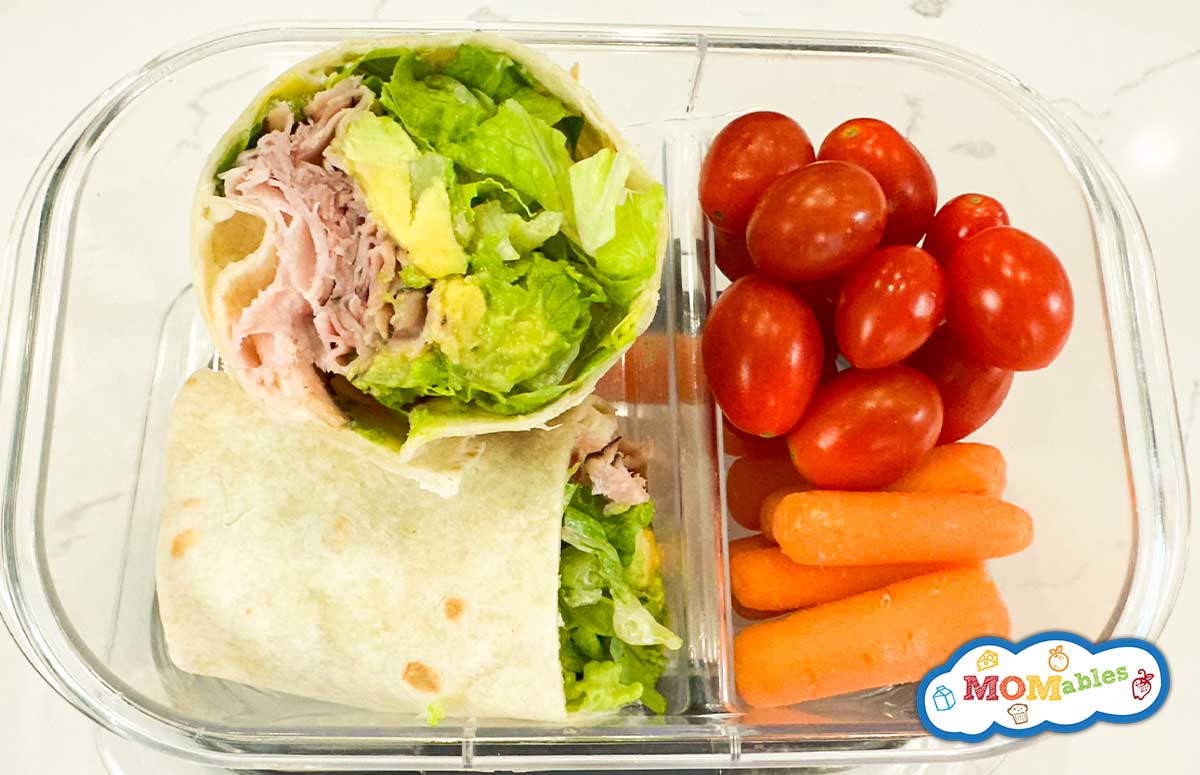 ham and avocado wrap in a lunchbox with cherry tomatoes and baby carrots