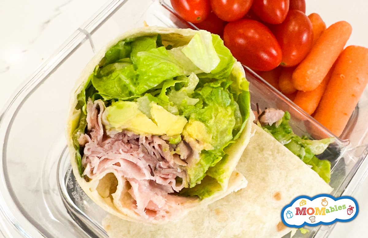 ham and avocado wrap in a lunchbox with cherry tomatoes and baby carrots