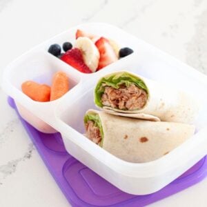 a healthy lunch made up of a bbq chicken wrap in a lunch box with berries and carrots in other compartments