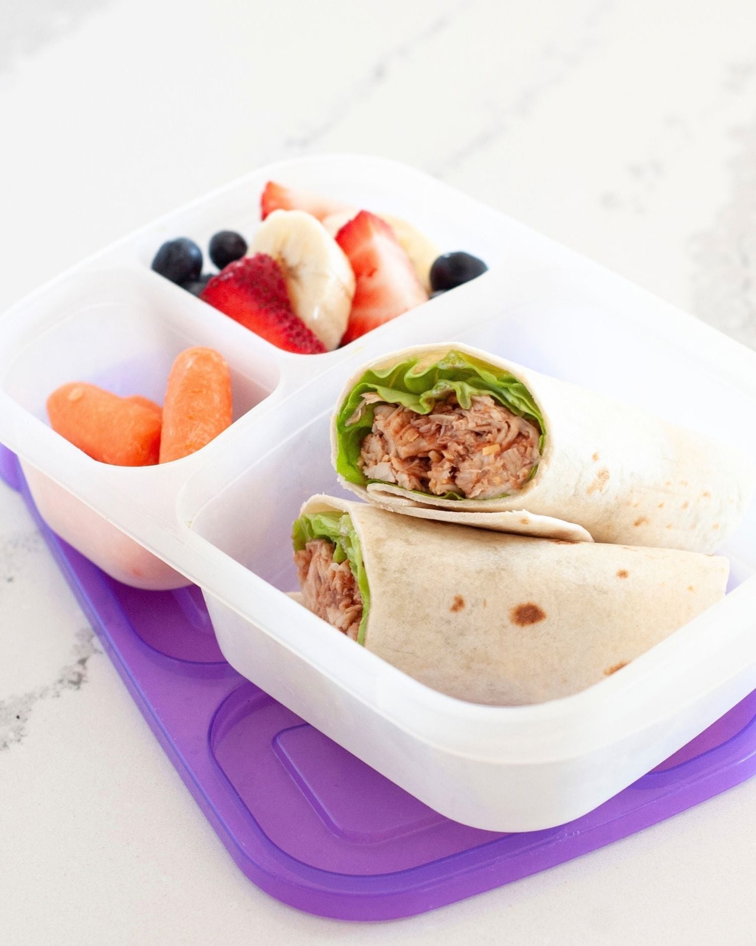 a healthy lunch made up of a bbq chicken wrap in a lunch box with berries and carrots in other compartments -full view