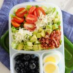 BLT salad in a lunch container with blueberries and two halves of a boiled egg