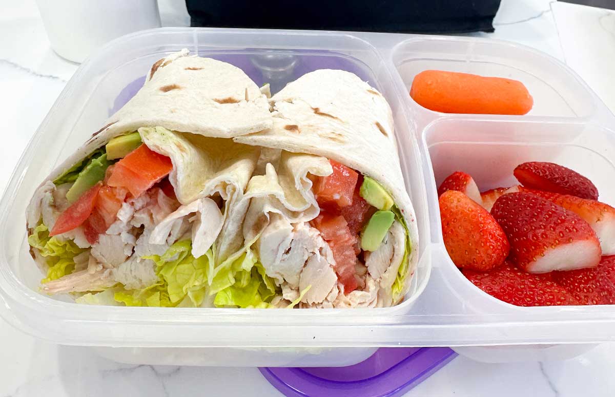 school lunch container with strawberries, baby carrots and a chicken avocado wrap