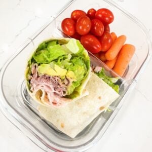 ham and avocado wrap in a lunchbox with cherry tomatoes and baby carrots