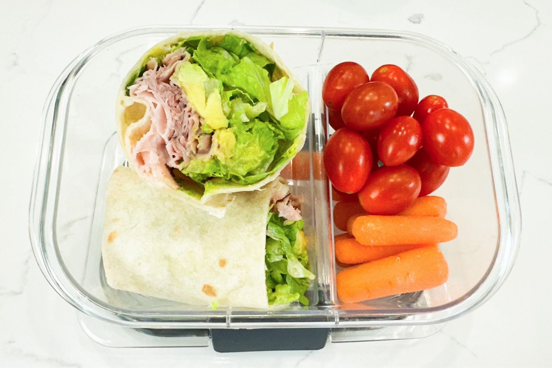 ham and avocado wrap in a lunchbox with cherry tomatoes and baby carrots