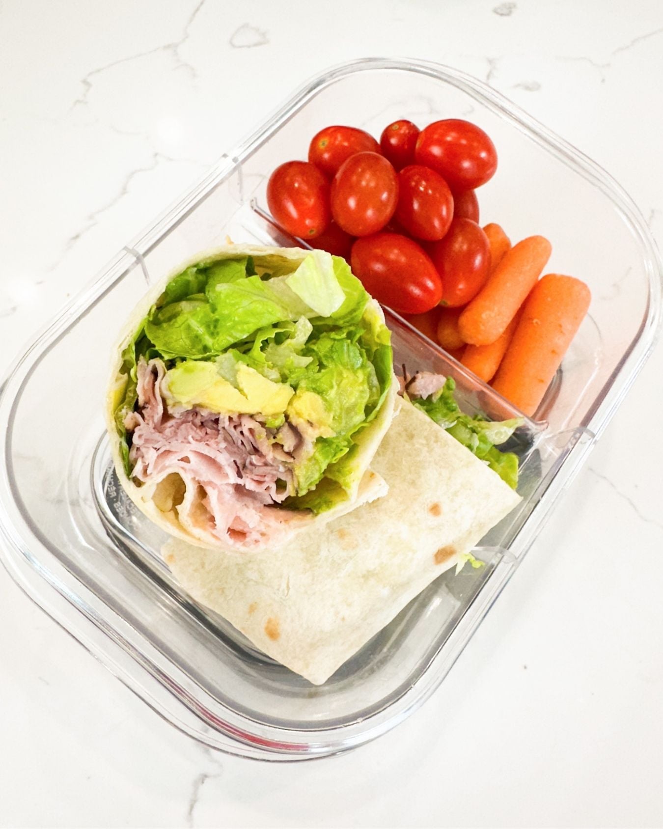 ham and avocado wrap in a lunchbox with cherry tomatoes and baby carrots