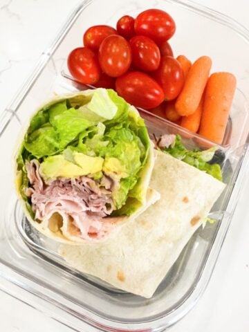 ham and avocado wrap in a lunchbox with cherry tomatoes and baby carrots
