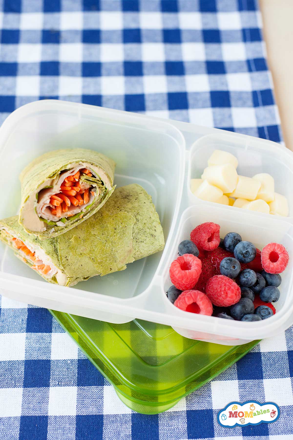 spinach wrap with turkey in a lunchbox with cheese cubes and berries on the side.