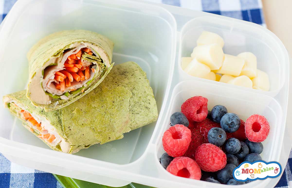 closeup of a lunch container with a spinach wrap and two lunch sides