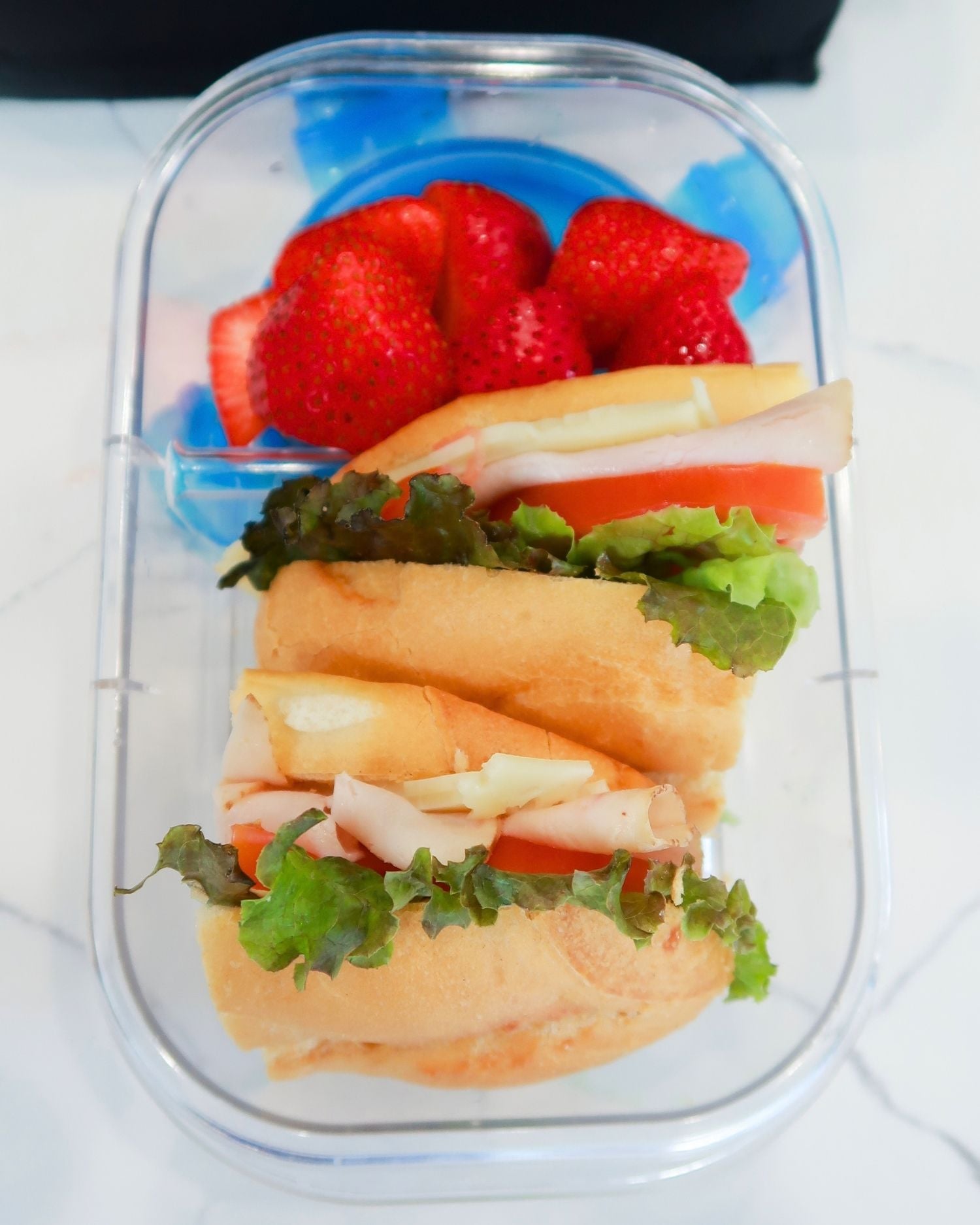 turkey sub sandwich sliced in halves in a lunchbox with fruit