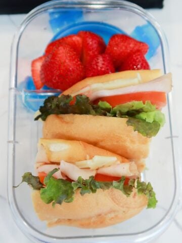 turkey sub sandwich sliced in halves in a lunchbox with fruit