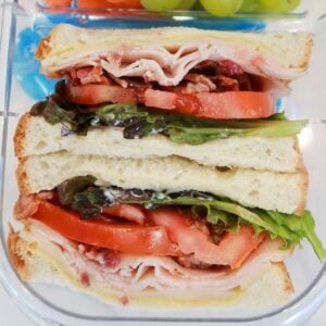 closeup of turkey sandwich with bacon, cheddar, tomato and lettuce in a lunchbox