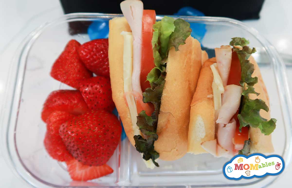 overhead view of turkey sub sandwich in a lunchbox with strawberries on the side