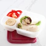 front view of a curry chicken salad wrap inside a lunch box packed with fruit and veggies on the side