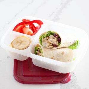 front view of a curry chicken salad wrap inside a lunch box packed with fruit and veggies on the side