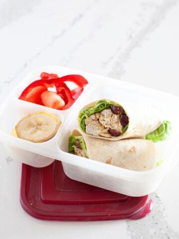 front view of a curry chicken salad wrap inside a lunch box packed with fruit and veggies on the side
