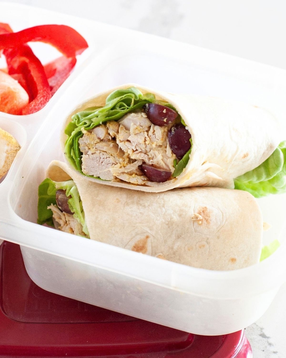 close up of a curry chicken salad wrap inside a lunch box packed with fruit and veggies on the side