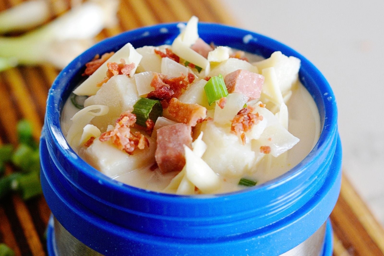 blue thermos filled with potato soup, and topped with bacon