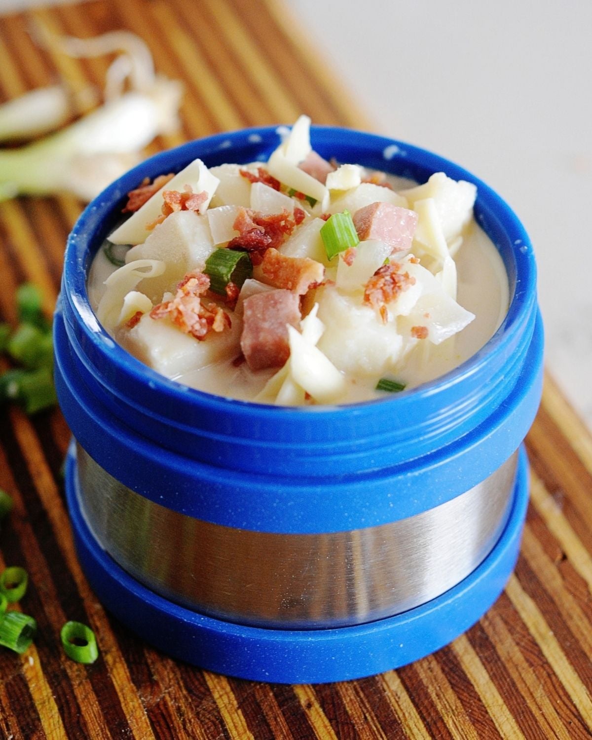blue thermos filled with potato soup, and topped with bacon