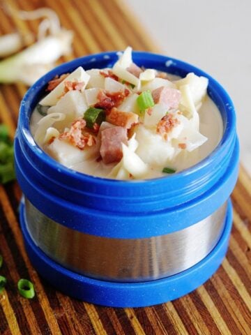 blue thermos filled with potato soup, and topped with bacon