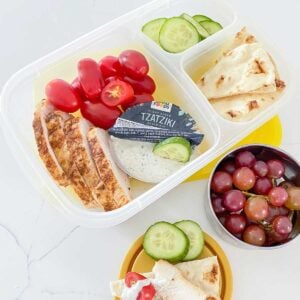 greek chicken bento box with veggies, fruit, and tzatziki sauce.