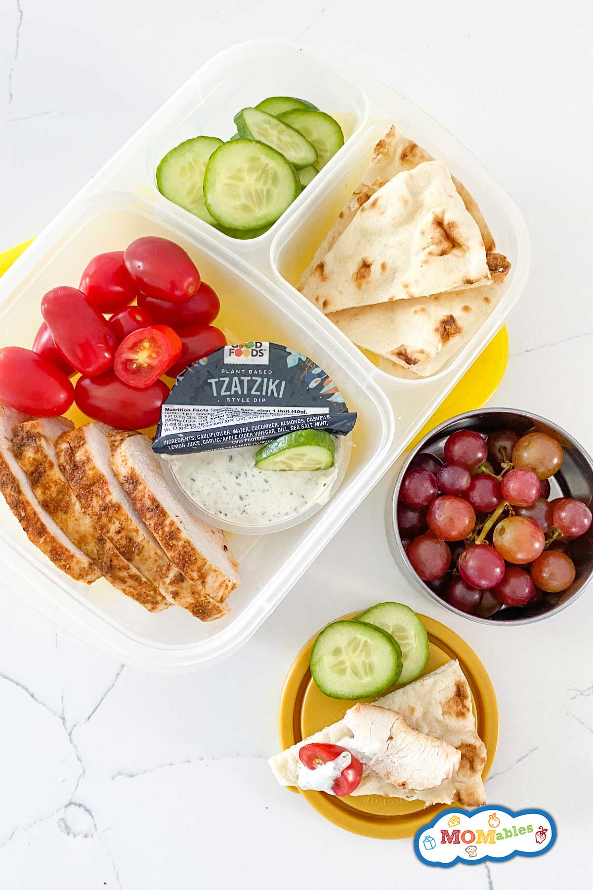 greek chicken bento box with veggies, fruit, and tzatziki sauce.