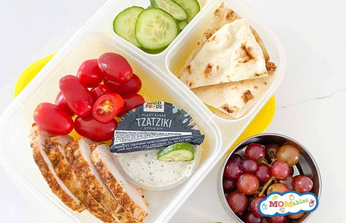 greek chicken bento box with veggies, fruit, and tzatziki sauce.