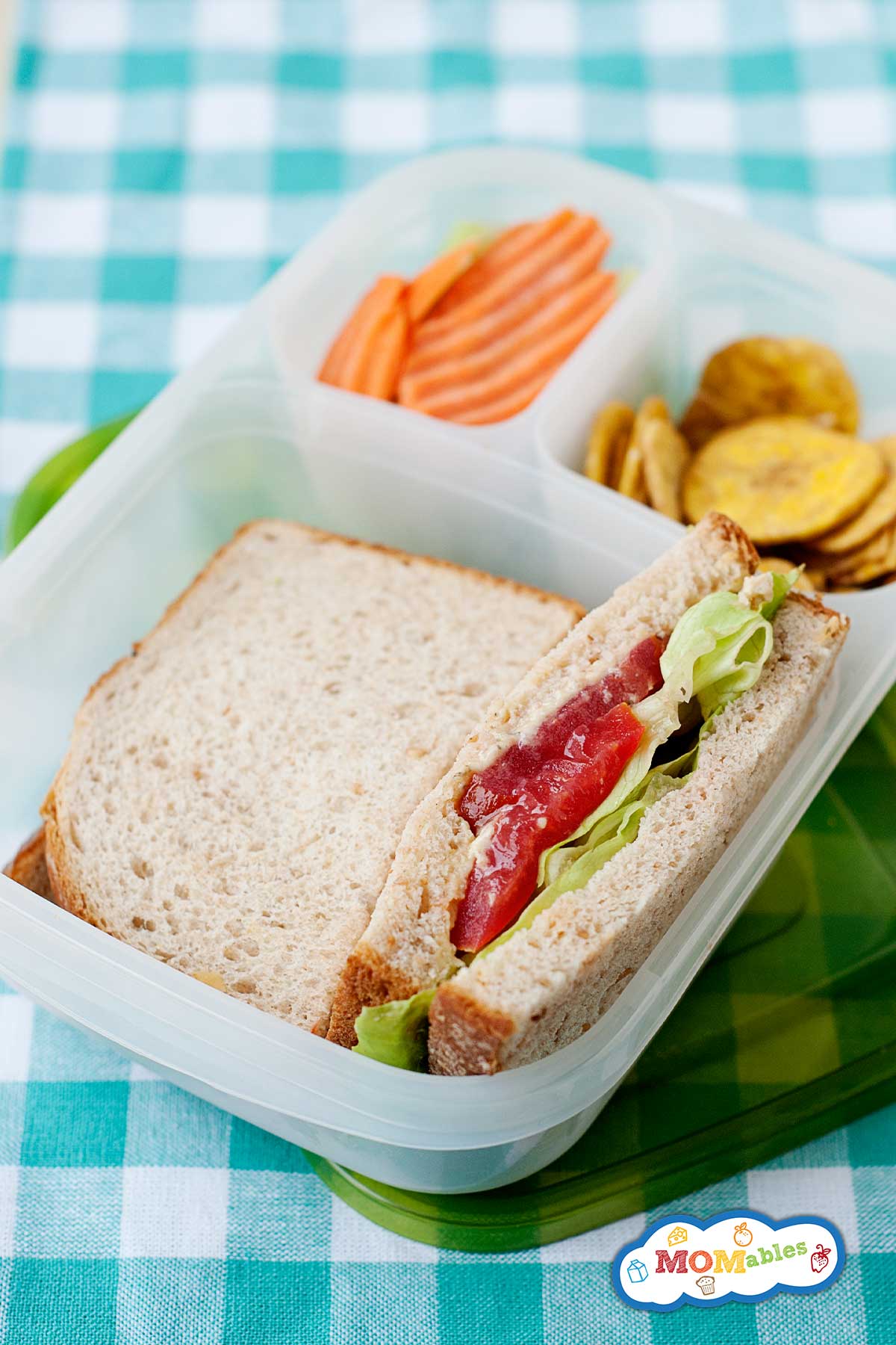hummus lettuce tomato sandwich in a lunchbox with banana chips and carrots