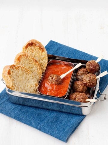 lunchbox with meatball skewers, tomato sauce and sliced bread