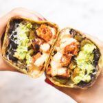 two hands holding halves of a chipotle chicken wrap