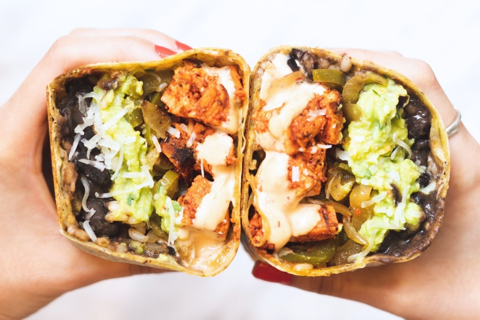 two hands holding halves of a chipotle chicken wrap