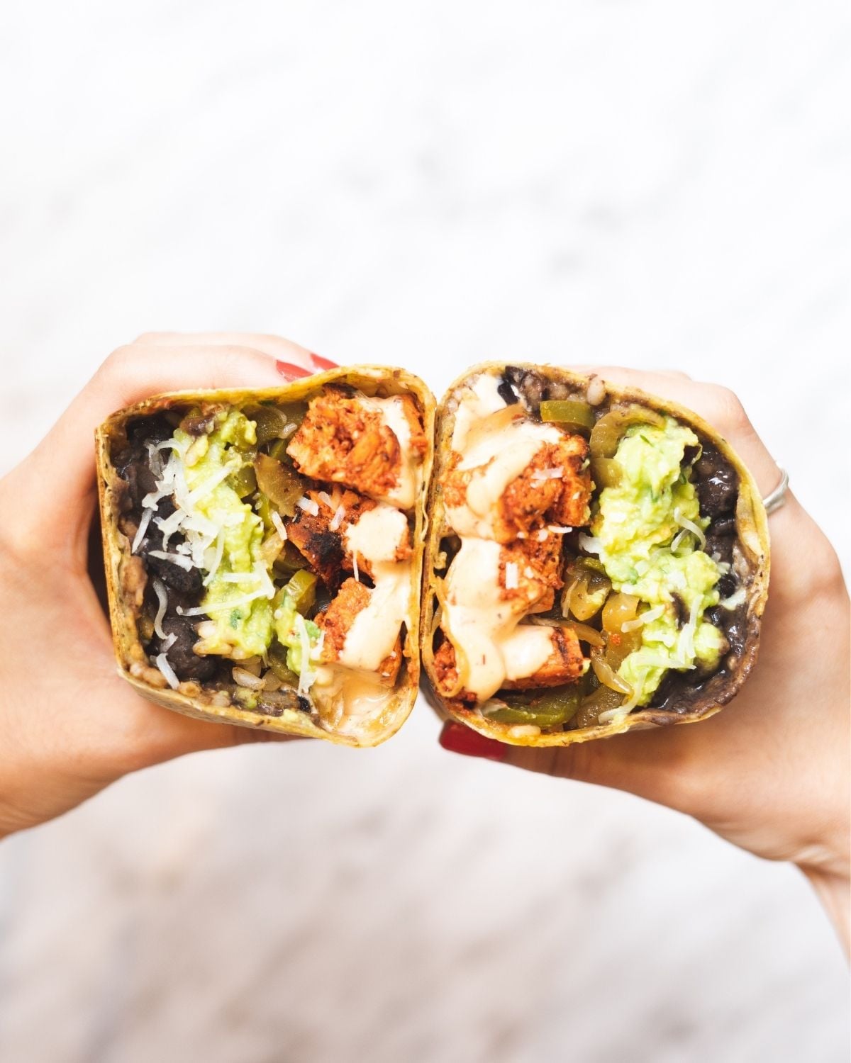 two hands holding halves of a chipotle chicken wrap