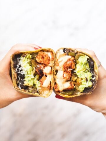 two hands holding halves of a chipotle chicken wrap
