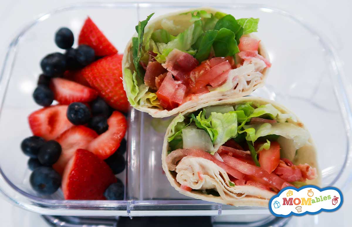 BLT wraps in a lunchbox with blueberries and strawberries on the side