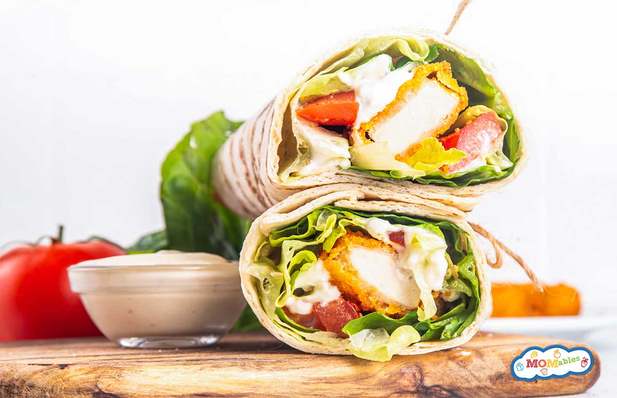 two chicken nugget wraps on a cutting board with veggies and salad dressing