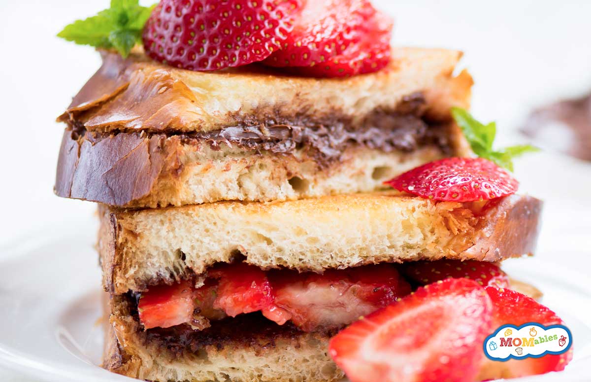 two halves of a strawberry nutella sandwich on a plate with more strawberries