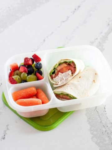 canned chicken wrap in a lunch container with veggies and fresh fruit