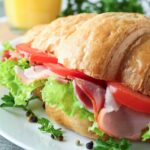 Ham and tomato croissant sandwich with lettuce on a plate.