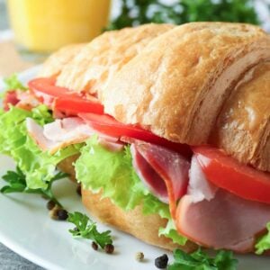 Ham and tomato croissant sandwich with lettuce on a plate.