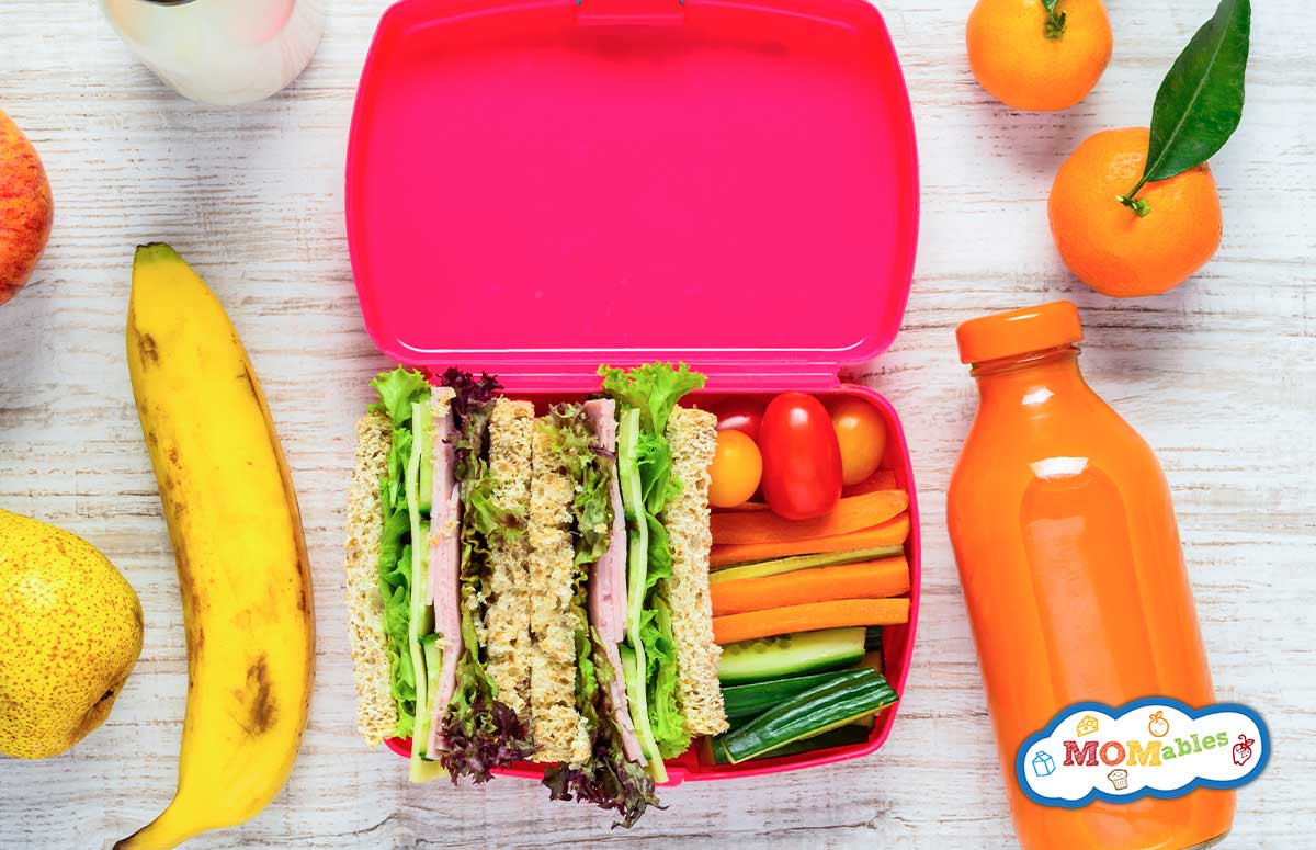 Two halves of a ham and cucumber sandwich in a lunchbox with cherry tomatoes, carrot sticks and cucumber sticks.