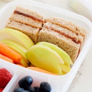 two peanut butter and jelly sandwich pieces in a lunch container with fruit